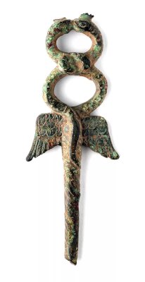A small caduceus made of dark bronze with green and rust patina. Two scaly snakes with crests on their heads twist into a knotted figure-8, kissing at the top. One of their tails wriggles down the staff. A pair of large, stylistic wings spreads out beneath them. The staff is tapered.