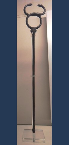 Bronze kerykeion on museum display. It is a tall, simple rod with a terminal at the bottom. The top curves up into a circular loop and crescent shape that ends in snake heads which are staring at each other.