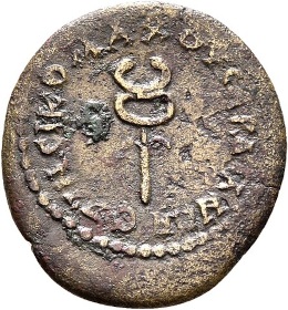 An irregular shaped brass colored coin, heavily worn with patina, showing a caduceus in the middle of a ring and circular legend that is illegible. The caduceus is a staff with small, faintly visible wings towards the top, an oblong oval over the top of the staff, and squashed horseshoe shape above that.