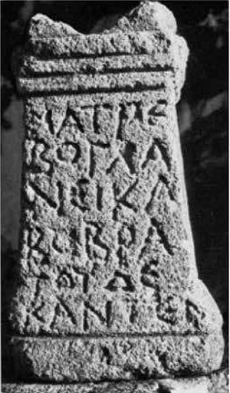 A grainy, black and white photo of the altar to the Glanican Mothers. It is a simple, stone, slightly trapezoidal altar inscribed from top to bottom in bold, rustic Greek capitals. It is heavily worn.